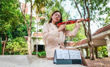 Genç bir Asyalı kadın bereketli yeşilliklerle çevrili huzurlu bir açık hava ortamında kibarca keman çalıyor. Doğada bir müzik konsantrasyonu ve sükunet anı yakalıyorum..