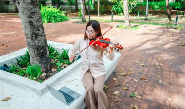 Genç bir Asyalı kadın bereketli yeşilliklerle çevrili huzurlu bir açık hava ortamında kibarca keman çalıyor. Doğada bir müzik konsantrasyonu ve sükunet anı yakalıyorum..