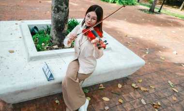 Genç bir Asyalı kadın bereketli yeşilliklerle çevrili huzurlu bir açık hava ortamında kibarca keman çalıyor. Doğada bir müzik konsantrasyonu ve sükunet anı yakalıyorum..