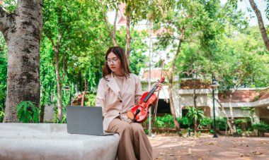 Genç bir Asyalı kadın bereketli yeşilliklerle çevrili huzurlu bir açık hava ortamında kibarca keman çalıyor. Doğada bir müzik konsantrasyonu ve sükunet anı yakalıyorum..