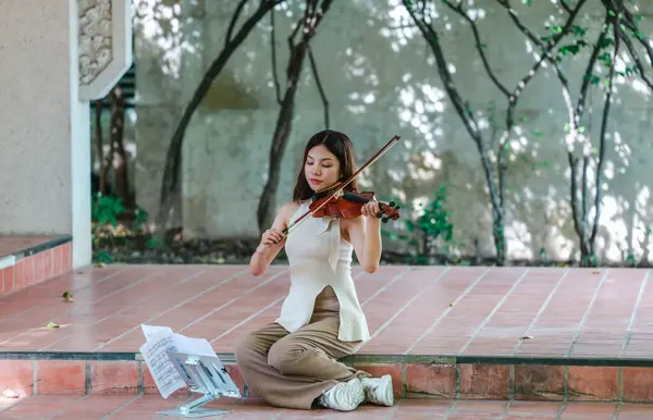 Genç bir Asyalı kadın bereketli yeşilliklerle çevrili huzurlu bir açık hava ortamında kibarca keman çalıyor. Doğada bir müzik konsantrasyonu ve sükunet anı yakalıyorum..