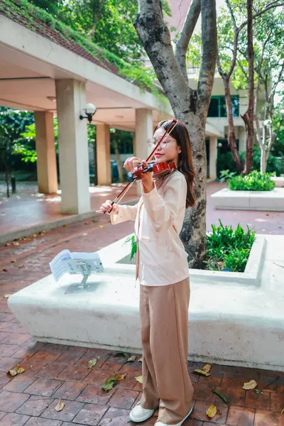 Genç bir Asyalı kadın bereketli yeşilliklerle çevrili huzurlu bir açık hava ortamında kibarca keman çalıyor. Doğada bir müzik konsantrasyonu ve sükunet anı yakalıyorum..