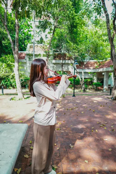 Genç bir Asyalı kadın bereketli yeşilliklerle çevrili huzurlu bir açık hava ortamında kibarca keman çalıyor. Doğada bir müzik konsantrasyonu ve sükunet anı yakalıyorum..