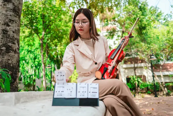 Genç bir Asyalı kadın bereketli yeşilliklerle çevrili huzurlu bir açık hava ortamında kibarca keman çalıyor. Doğada bir müzik konsantrasyonu ve sükunet anı yakalıyorum..