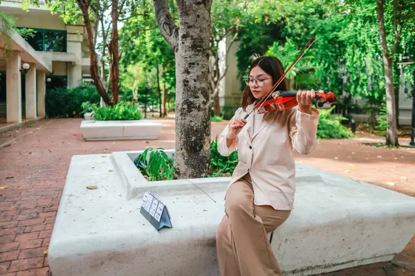 Genç bir Asyalı kadın bereketli yeşilliklerle çevrili huzurlu bir açık hava ortamında kibarca keman çalıyor. Doğada bir müzik konsantrasyonu ve sükunet anı yakalıyorum..