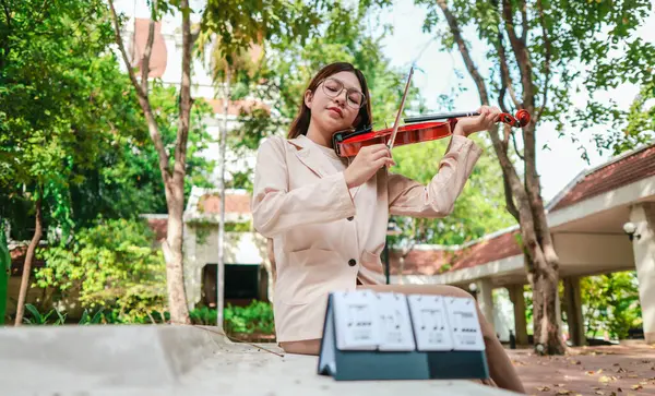 Genç bir Asyalı kadın bereketli yeşilliklerle çevrili huzurlu bir açık hava ortamında kibarca keman çalıyor. Doğada bir müzik konsantrasyonu ve sükunet anı yakalıyorum..