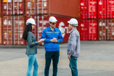 Kadın yönetici, konteyner deposunda iki erkek işçiyle lojistiği denetliyor ve tartışıyor. Küresel ticaret ve ulaşım endüstrisinin altını çizmek için toplanmış konteynırlar ve endüstriyel ekipmanlar