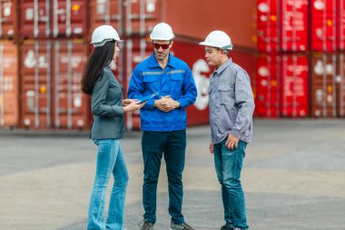 Kadın yönetici, konteyner deposunda iki erkek işçiyle lojistiği denetliyor ve tartışıyor. Küresel ticaret ve ulaşım endüstrisinin altını çizmek için toplanmış konteynırlar ve endüstriyel ekipmanlar