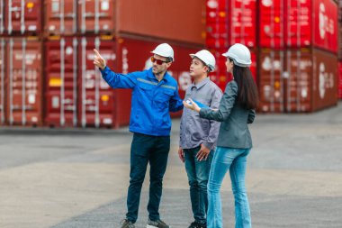Kadın yönetici, konteyner deposunda iki erkek işçiyle lojistiği denetliyor ve tartışıyor. Küresel ticaret ve ulaşım endüstrisinin altını çizmek için toplanmış konteynırlar ve endüstriyel ekipmanlar