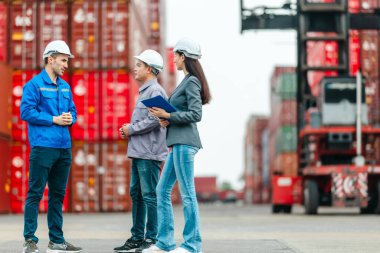 Kadın yönetici, konteyner deposunda iki erkek işçiyle lojistiği denetliyor ve tartışıyor. Küresel ticaret ve ulaşım endüstrisinin altını çizmek için toplanmış konteynırlar ve endüstriyel ekipmanlar