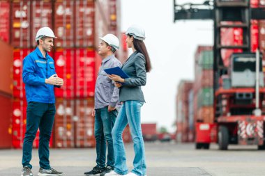 Kadın yönetici, konteyner deposunda iki erkek işçiyle lojistiği denetliyor ve tartışıyor. Küresel ticaret ve ulaşım endüstrisinin altını çizmek için toplanmış konteynırlar ve endüstriyel ekipmanlar