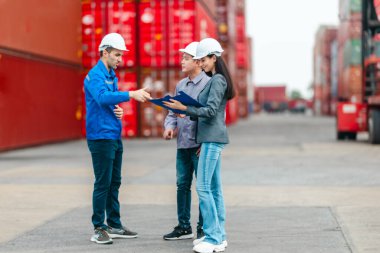 Kadın yönetici, konteyner deposunda iki erkek işçiyle lojistiği denetliyor ve tartışıyor. Küresel ticaret ve ulaşım endüstrisinin altını çizmek için toplanmış konteynırlar ve endüstriyel ekipmanlar
