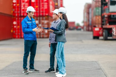 Kadın yönetici, konteyner deposunda iki erkek işçiyle lojistiği denetliyor ve tartışıyor. Küresel ticaret ve ulaşım endüstrisinin altını çizmek için toplanmış konteynırlar ve endüstriyel ekipmanlar
