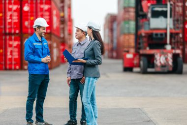 Kadın yönetici, konteyner deposunda iki erkek işçiyle lojistiği denetliyor ve tartışıyor. Küresel ticaret ve ulaşım endüstrisinin altını çizmek için toplanmış konteynırlar ve endüstriyel ekipmanlar