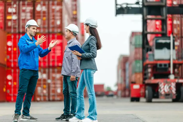 Kadın yönetici, konteyner deposunda iki erkek işçiyle lojistiği denetliyor ve tartışıyor. Küresel ticaret ve ulaşım endüstrisinin altını çizmek için toplanmış konteynırlar ve endüstriyel ekipmanlar