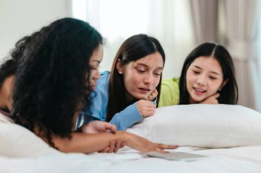 Bir grup farklı genç kadın bir yatakta uzanıyor, rahat, iyi ışıklandırılmış bir yatak odası ortamında dijital bir oyunla neşeyle meşgul oluyorlar. Görüntü arkadaşlığı, eğlenceyi ve olumlu bağlantıyı yakalıyor..