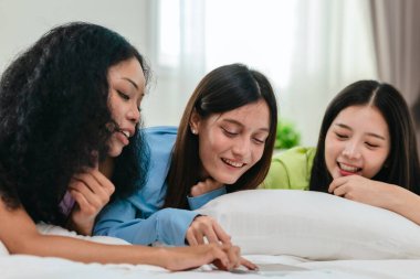 Bir grup farklı genç kadın bir yatakta uzanıyor, rahat, iyi ışıklandırılmış bir yatak odası ortamında dijital bir oyunla neşeyle meşgul oluyorlar. Görüntü arkadaşlığı, eğlenceyi ve olumlu bağlantıyı yakalıyor..