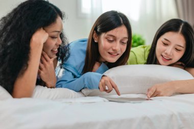 Bir grup farklı genç kadın bir yatakta uzanıyor, rahat, iyi ışıklandırılmış bir yatak odası ortamında dijital bir oyunla neşeyle meşgul oluyorlar. Görüntü arkadaşlığı, eğlenceyi ve olumlu bağlantıyı yakalıyor..