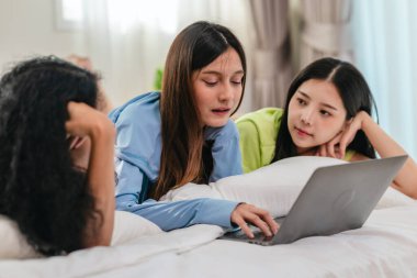 Bir grup farklı genç kadın bir yatakta uzanıyor, rahat, iyi ışıklandırılmış bir yatak odası ortamında dijital bir oyunla neşeyle meşgul oluyorlar. Görüntü arkadaşlığı, eğlenceyi ve olumlu bağlantıyı yakalıyor..