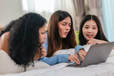 Bir grup farklı genç kadın bir yatakta uzanıyor, rahat, iyi ışıklandırılmış bir yatak odası ortamında dijital bir oyunla neşeyle meşgul oluyorlar. Görüntü arkadaşlığı, eğlenceyi ve olumlu bağlantıyı yakalıyor..