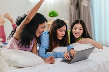 Bir grup farklı genç kadın bir yatakta uzanıyor, rahat, iyi ışıklandırılmış bir yatak odası ortamında dijital bir oyunla neşeyle meşgul oluyorlar. Görüntü arkadaşlığı, eğlenceyi ve olumlu bağlantıyı yakalıyor..