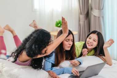 Bir grup farklı genç kadın bir yatakta uzanıyor, rahat, iyi ışıklandırılmış bir yatak odası ortamında dijital bir oyunla neşeyle meşgul oluyorlar. Görüntü arkadaşlığı, eğlenceyi ve olumlu bağlantıyı yakalıyor..