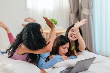 Bir grup farklı genç kadın bir yatakta uzanıyor, rahat, iyi ışıklandırılmış bir yatak odası ortamında dijital bir oyunla neşeyle meşgul oluyorlar. Görüntü arkadaşlığı, eğlenceyi ve olumlu bağlantıyı yakalıyor..