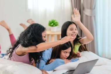 Bir grup farklı genç kadın bir yatakta uzanıyor, rahat, iyi ışıklandırılmış bir yatak odası ortamında dijital bir oyunla neşeyle meşgul oluyorlar. Görüntü arkadaşlığı, eğlenceyi ve olumlu bağlantıyı yakalıyor..