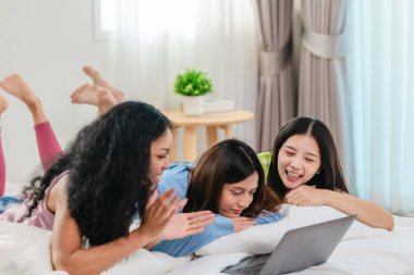 Bir grup farklı genç kadın bir yatakta uzanıyor, rahat, iyi ışıklandırılmış bir yatak odası ortamında dijital bir oyunla neşeyle meşgul oluyorlar. Görüntü arkadaşlığı, eğlenceyi ve olumlu bağlantıyı yakalıyor..