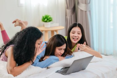 Bir grup farklı genç kadın bir yatakta uzanıyor, rahat, iyi ışıklandırılmış bir yatak odası ortamında dijital bir oyunla neşeyle meşgul oluyorlar. Görüntü arkadaşlığı, eğlenceyi ve olumlu bağlantıyı yakalıyor..