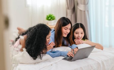 Bir grup farklı genç kadın bir yatakta uzanıyor, rahat, iyi ışıklandırılmış bir yatak odası ortamında dijital bir oyunla neşeyle meşgul oluyorlar. Görüntü arkadaşlığı, eğlenceyi ve olumlu bağlantıyı yakalıyor..