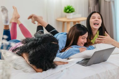 Bir grup farklı genç kadın bir yatakta uzanıyor, rahat, iyi ışıklandırılmış bir yatak odası ortamında dijital bir oyunla neşeyle meşgul oluyorlar. Görüntü arkadaşlığı, eğlenceyi ve olumlu bağlantıyı yakalıyor..