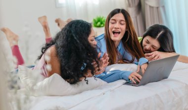 Bir grup farklı genç kadın bir yatakta uzanıyor, rahat, iyi ışıklandırılmış bir yatak odası ortamında dijital bir oyunla neşeyle meşgul oluyorlar. Görüntü arkadaşlığı, eğlenceyi ve olumlu bağlantıyı yakalıyor..