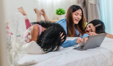 Bir grup farklı genç kadın bir yatakta uzanıyor, rahat, iyi ışıklandırılmış bir yatak odası ortamında dijital bir oyunla neşeyle meşgul oluyorlar. Görüntü arkadaşlığı, eğlenceyi ve olumlu bağlantıyı yakalıyor..