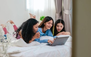 Bir grup farklı genç kadın bir yatakta uzanıyor, rahat, iyi ışıklandırılmış bir yatak odası ortamında dijital bir oyunla neşeyle meşgul oluyorlar. Görüntü arkadaşlığı, eğlenceyi ve olumlu bağlantıyı yakalıyor..