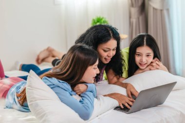 Bir grup farklı genç kadın bir yatakta uzanıyor, rahat, iyi ışıklandırılmış bir yatak odası ortamında dijital bir oyunla neşeyle meşgul oluyorlar. Görüntü arkadaşlığı, eğlenceyi ve olumlu bağlantıyı yakalıyor..