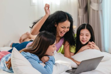 Bir grup farklı genç kadın bir yatakta uzanıyor, rahat, iyi ışıklandırılmış bir yatak odası ortamında dijital bir oyunla neşeyle meşgul oluyorlar. Görüntü arkadaşlığı, eğlenceyi ve olumlu bağlantıyı yakalıyor..