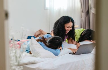 Bir grup farklı genç kadın bir yatakta uzanıyor, rahat, iyi ışıklandırılmış bir yatak odası ortamında dijital bir oyunla neşeyle meşgul oluyorlar. Görüntü arkadaşlığı, eğlenceyi ve olumlu bağlantıyı yakalıyor..