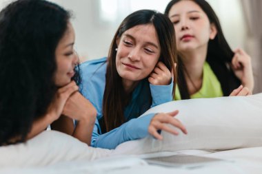 Bir grup farklı genç kadın bir yatakta uzanıyor, rahat, iyi ışıklandırılmış bir yatak odası ortamında dijital bir oyunla neşeyle meşgul oluyorlar. Görüntü arkadaşlığı, eğlenceyi ve olumlu bağlantıyı yakalıyor..