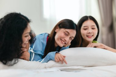 Bir grup farklı genç kadın bir yatakta uzanıyor, rahat, iyi ışıklandırılmış bir yatak odası ortamında dijital bir oyunla neşeyle meşgul oluyorlar. Görüntü arkadaşlığı, eğlenceyi ve olumlu bağlantıyı yakalıyor..