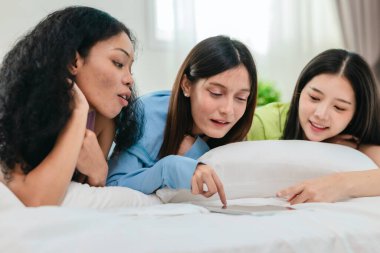 Bir grup farklı genç kadın bir yatakta uzanıyor, rahat, iyi ışıklandırılmış bir yatak odası ortamında dijital bir oyunla neşeyle meşgul oluyorlar. Görüntü arkadaşlığı, eğlenceyi ve olumlu bağlantıyı yakalıyor..