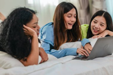 Bir grup farklı genç kadın bir yatakta uzanıyor, rahat, iyi ışıklandırılmış bir yatak odası ortamında dijital bir oyunla neşeyle meşgul oluyorlar. Görüntü arkadaşlığı, eğlenceyi ve olumlu bağlantıyı yakalıyor..