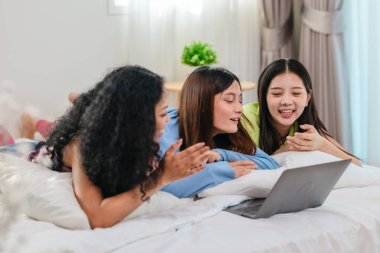 Bir grup farklı genç kadın bir yatakta uzanıyor, rahat, iyi ışıklandırılmış bir yatak odası ortamında dijital bir oyunla neşeyle meşgul oluyorlar. Görüntü arkadaşlığı, eğlenceyi ve olumlu bağlantıyı yakalıyor..