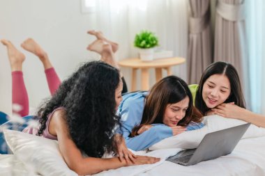 Bir grup farklı genç kadın bir yatakta uzanıyor, rahat, iyi ışıklandırılmış bir yatak odası ortamında dijital bir oyunla neşeyle meşgul oluyorlar. Görüntü arkadaşlığı, eğlenceyi ve olumlu bağlantıyı yakalıyor..