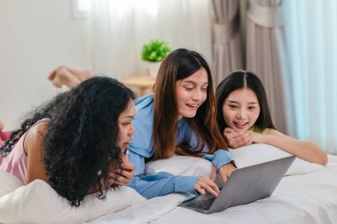 Bir grup farklı genç kadın bir yatakta uzanıyor, rahat, iyi ışıklandırılmış bir yatak odası ortamında dijital bir oyunla neşeyle meşgul oluyorlar. Görüntü arkadaşlığı, eğlenceyi ve olumlu bağlantıyı yakalıyor..