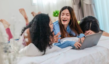 Bir grup farklı genç kadın bir yatakta uzanıyor, rahat, iyi ışıklandırılmış bir yatak odası ortamında dijital bir oyunla neşeyle meşgul oluyorlar. Görüntü arkadaşlığı, eğlenceyi ve olumlu bağlantıyı yakalıyor..