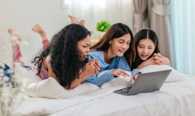 Bir grup farklı genç kadın bir yatakta uzanıyor, rahat, iyi ışıklandırılmış bir yatak odası ortamında dijital bir oyunla neşeyle meşgul oluyorlar. Görüntü arkadaşlığı, eğlenceyi ve olumlu bağlantıyı yakalıyor..