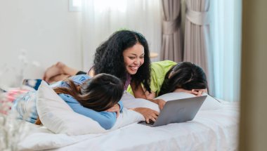 Bir grup farklı genç kadın bir yatakta uzanıyor, rahat, iyi ışıklandırılmış bir yatak odası ortamında dijital bir oyunla neşeyle meşgul oluyorlar. Görüntü arkadaşlığı, eğlenceyi ve olumlu bağlantıyı yakalıyor..