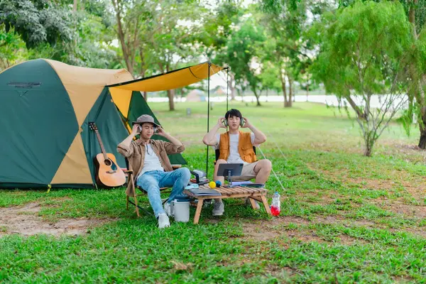 İki Asyalı erkek arkadaş gölün kenarında dinleniyor, müziğin tadını çıkarıyor ve açık hava ortamında birlikte şarkı söylüyorlar. Sahne, kamp gezisi sırasında neşeli ve huzurlu bir bağ ve yaratıcılık anı yakalıyor.