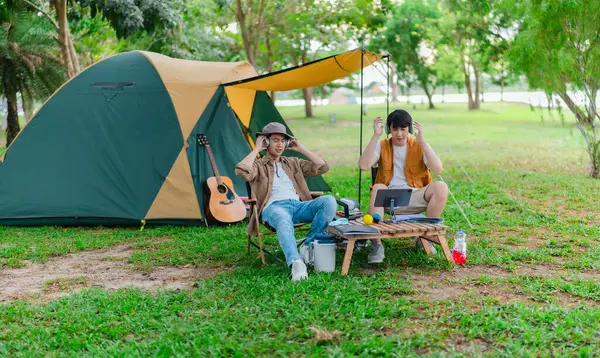 İki Asyalı erkek arkadaş gölün kenarında dinleniyor, müziğin tadını çıkarıyor ve açık hava ortamında birlikte şarkı söylüyorlar. Sahne, kamp gezisi sırasında neşeli ve huzurlu bir bağ ve yaratıcılık anı yakalıyor.